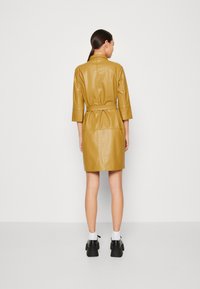 Abito in pelle giallo senape con design colletto, maniche a tre quarti, vita cintata e taglio dritto, visto da dietro.