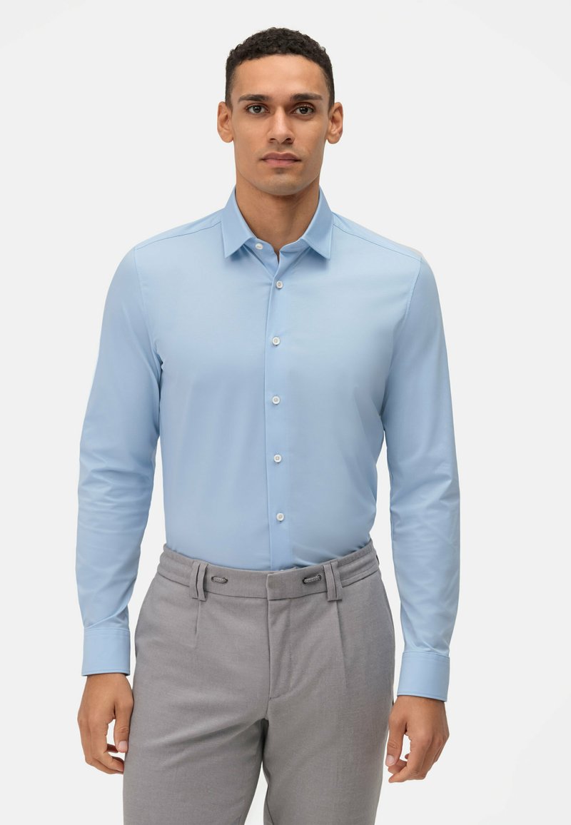 Lichtblauw overhemd met lange mouwen en een button-down kraag, voorzien van witte knopen, gecombineerd met grijze broeken met een geplooide voorkant en zijknopen.