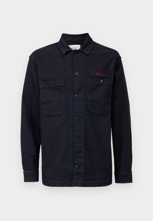 Cămașă din denim albastru închis, cu mâneci lungi, închidere cu nasturi, două buzunare pe piept și un mic logo roșu "REPLAY" pe buzunarul din stânga.