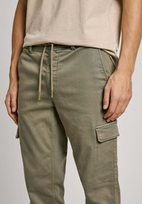 Pantalones cargo color caqui con un ajuste relajado, que cuentan con una cinturilla ajustable y bolsillos laterales. La tela tiene una textura suave con un brillo sutil.
