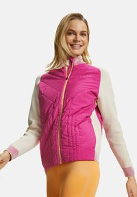 Rosa isolierte Jacke mit cremefarbenen Ärmeln, Reißverschluss, gemusterten Bündchen und gestepptem Design auf der Vorderseite. Orange Leggings sind sichtbar.