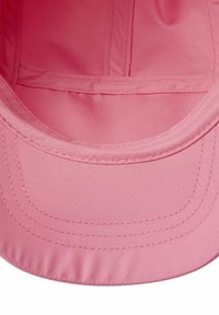 Rosa tygkaps med en böjd skärm, slät textur och detaljerad sömnad längs kanterna och sömmarna. Insidan är klädd med mjukt material.