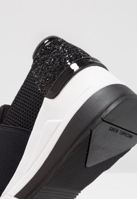 Sneaker nera con tomaia in rete testurizzata e un accento glitterato nero sul tallone. Presenta una suola intermedia bianca spessa e una suola in gomma con motivo.