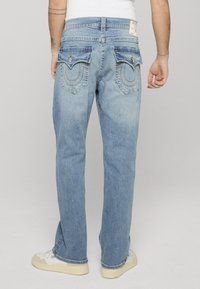 Vaqueros de mezclilla de lavado claro con corte de pierna recta, que presentan dos bolsillos con solapa y costuras decorativas en los bolsillos traseros.