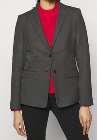 Grå mønstrede blazer har en skræddersyet pasform, klaplukninger, to knapper og sidelommer, båret over en rød ribbet sweater.