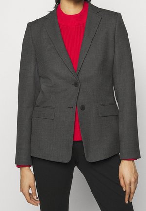 Grå mønstrede blazer har en skræddersyet pasform, klaplukninger, to knapper og sidelommer, båret over en rød ribbet sweater.