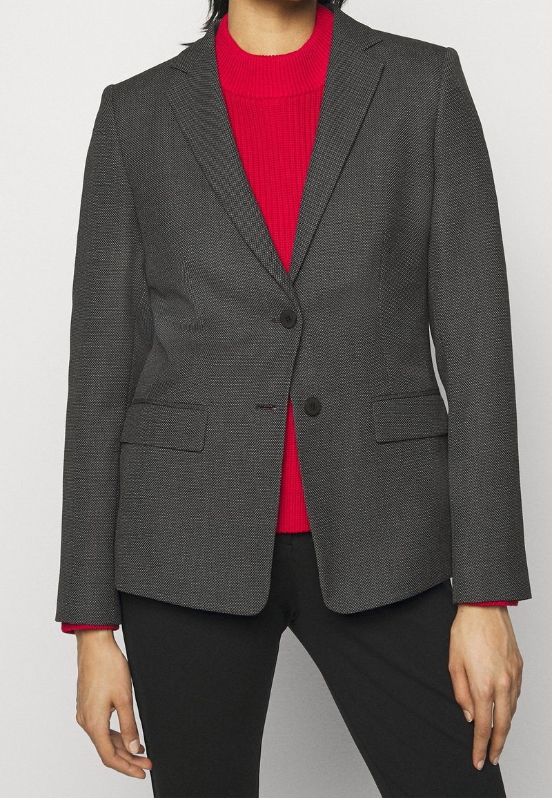 Grå mønstrede blazer har en skræddersyet pasform, klaplukninger, to knapper og sidelommer, båret over en rød ribbet sweater.