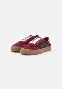 Paire de baskets en daim bordeaux avec semelles en gomme, lacets blancs, détail latéral noir et accents roses au talon sur fond blanc.
