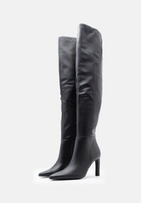 Botas de cuero negras hasta la rodilla, con punta afilada, tacón de aguja, textura suave y detalle de cremallera lateral para facilitar su uso.