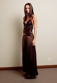 Bruin pailletten top met bloemmotief, gecombineerd met een vloeiende, donkerbruine rok. Strakke, aansluitende silhouet met subtiele textuur. Klassieke zwarte hakken.