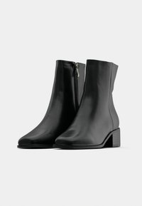 Bottines en cuir noir à texture lisse, avec un bout arrondi et un talon bloc bas. Elles disposent d'une fermeture éclair latérale pour un enfilage facile.