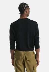 Pull en tricot noir avec un col rond et des manches longues, associé à un pantalon cargo vert olive avec des poches plaquées et des accents de boutons.