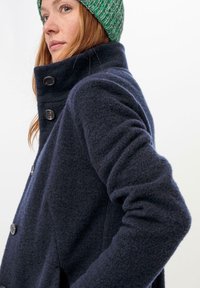 Abrigo de lana navy con un cuello alto, que cuenta con cuatro botones y un tejido texturizado, detallado con un acabado suave y cepillado.