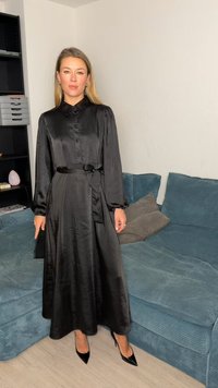 Μαύρο μίντι φόρεμα από σατέν με μακριά μανίκια, ρεγκλάν με κουμπιά και ζώνη δετή στη μέση. Λαμπερή υφή και αέρινη σιλουέτα. Μαύρες μυτερές γόβες.