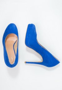 Modré semišové vysoké podpatky s hladkým povrchem, mandlovým tvarem špičky a štíhlým stiletto podpatkem. Interiér je vybaven světle hnědou podšívkou.