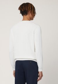Witte katoenen sweatshirt met een ronde halslijn, geribde manchetten en tailleband. Draagt bij navy broek, met een eenvoudig, recht achterontwerp.