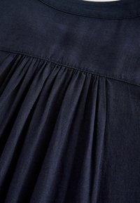 Tmavě námořnická tkanina s jemnými sklady, hladkou texturou a kulatým výstřihem, prezentující drapovaný design bez dalších detailů.