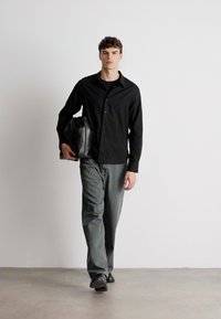 Musternööpide shirt, hallid teksad, mustad kingad. Mudel hoiab musta nahk-kotti. Lihtne disain, neutraalsetes värvides ja sirge lõikega.