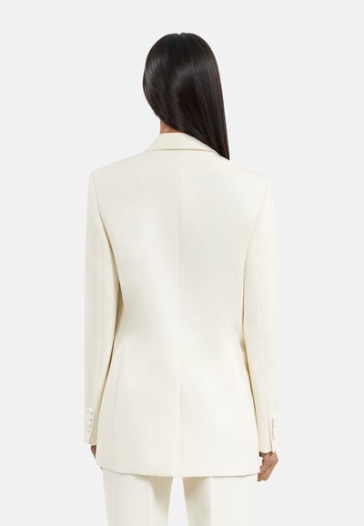 Blazer bianco strutturato con una vestibilità su misura, rever affilati e polsini bottone. La texture liscia e le linee pulite caratterizzano il design.