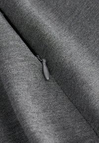 Tissu gris texturé avec un motif de tissage subtil et une tirette de fermeture éclair grise est partiellement visible, mettant en valeur la douceur et le design du matériau.
