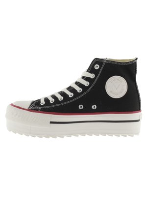Zapatillas altas negras con cordones blancos, puntera de goma y suela de plataforma a rayas. Presentan un parche con el logo y costuras en contraste.