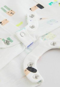 Vêtements pour bébé blancs avec boutons-pression, présentant un motif de visages d'animaux dessinés, incluant des ours et des chiens aux couleurs pastel.