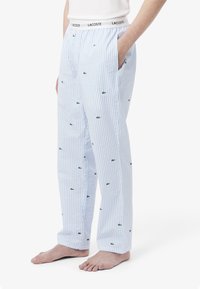 Lichtblauwe gestreepte pyjamabroek met groene Lacoste-logo's. Gemaakt van zachte stof met een elastische tailleband en zijzakken.