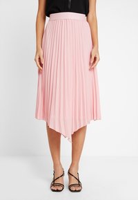 Vaaleanpunainen laskostettu hame, jossa on epäsymmetrinen helma, valmistettu kevyestä materiaalista. Sillä on leveä vyötärö ja se ulottuu puoliväliin pohkeita.