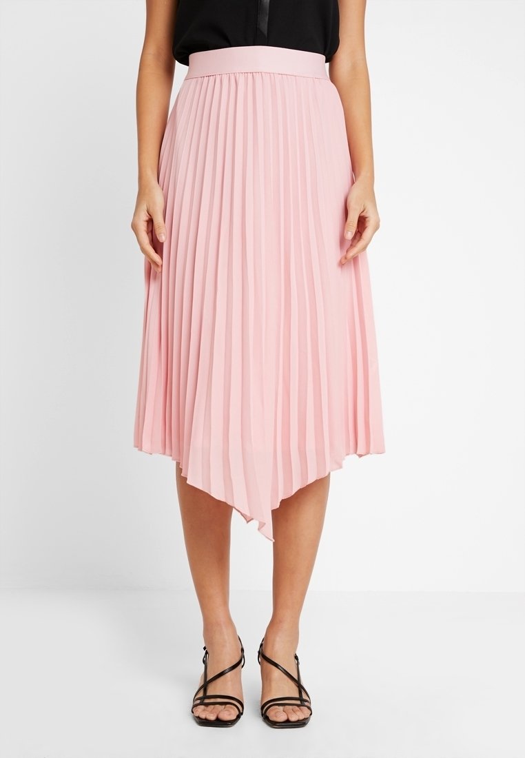 Vaaleanpunainen laskostettu hame, jossa on epäsymmetrinen helma, valmistettu kevyestä materiaalista. Sillä on leveä vyötärö ja se ulottuu puoliväliin pohkeita.