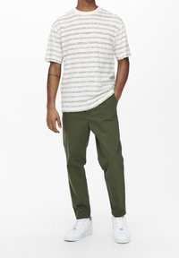 Pruhovaná košile s krátkými rukávy v bílé barvě se zelenými a modrými proužky, doplněná zelenými kalhotami a bílými teniskami. Volný střih a měkká textura.