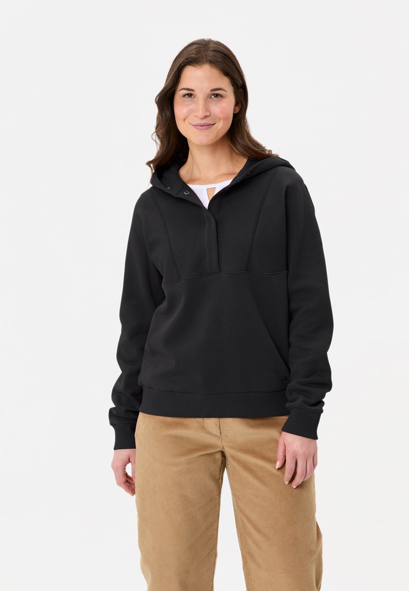 Felpa nera con cappuccio e apertura frontale, polsini e orlo a costine. Texture liscia, design aderente e cappuccio. Abbinata a pantaloni in velluto a coste marrone chiaro.