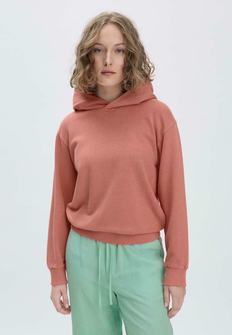 Hoodie in terracotta, casual pasvorm met ribbels aan de mouwen en onderkant. Draag het over mintgroene broek, zachte stof, minimalistisch ontwerp.