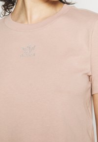 Ljusrosa bomulls-t-shirt med korta ärmar och rund halsringning; har en liten logotyp prydd med rhinstenar på br östet.