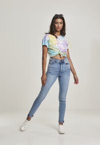 Kratký top s puntíky v pastelových barvách, v kombinaci s světle modrými úzkými džínami a bílými teniskami. Modelka stojí na neutrálním pozadí.
