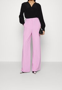 Top nero avvolgente con maniche lunghe abbinato a pantaloni rosa a vita alta e a gamba larga. Borsa nera e décolleté a punta bicolore.