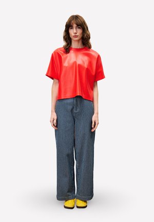 Rode, cropped nepleren top met korte mouwen, gecombineerd met blauw-wit gestreepte broek met wijde pijpen. Felgele sneakers maken de outfit compleet.