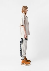 Camiseta beige de gran tamaño, joggers gris claro con parches en blanco y negro, y botas de tobillo marrones con cordones y suela gruesa.