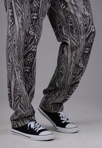 Person wearing black and white patterned pants and black canvas sneakers with white laces, standing against a plain background.