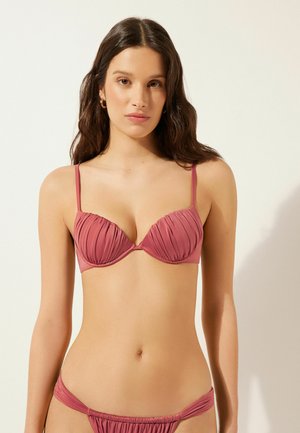 Pink padded bikini top with pleated texture and adjustable straps; matching pleated bikini bottom. Smooth fabric with minimal hardware accents.