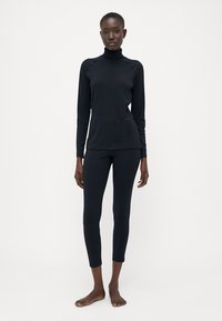Un pull à col roulé noir à manches longues associé à des leggings noirs arrivant aux chevilles. Les deux articles sont en tissu lisse et extensible.