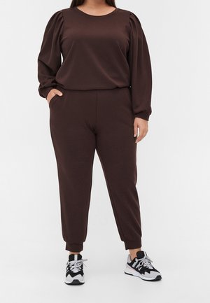 Felpa marrone e pantaloni jogger coordinati realizzati in tessuto morbido, con maniche a palloncino e polsini elasticizzati, abbinati a sneakers nere e bianche.