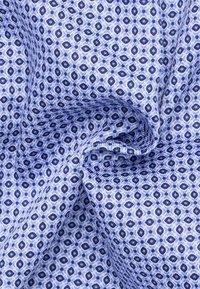 Lichtblauwe stof met een ruit- en ovale patroon in donkerblauw en wit, met een gladde textuur en ingewikkelde ontwerpdetails.