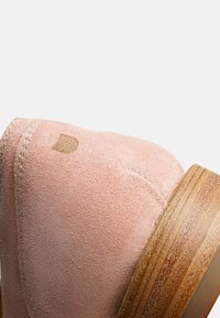 Rosa Wildleder-Stiefelette mit einer runden Zehenform, sichtbaren Nähten und einer Holzsohle. Mit einem kleinen Logodetail in der Nähe der Ferse.