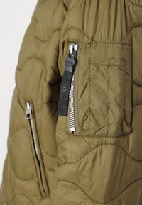Olive zaļš quilted jaka ar metāliskiem rāvējslēdzējiem, plākšņu kabatu un teksturētu audumu. Iespējas ietver logotipu uz rāvējslēdzēja vilkšanas un elegantu dizainu.