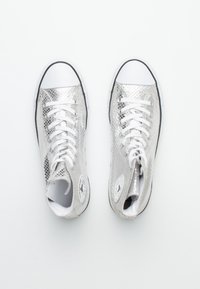 Pár stříbrných metalických vysokých tenisek s bílými tkaničkami a špičkami, zobrazených shora na bílém pozadí.