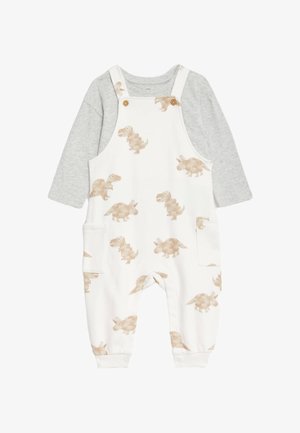 Białe ogrodniczki z beżowymi nadrukami dinozaurów, z szarym długim rękawem pod spodem. Wykonane z miękkiej bawełny, zawierają kieszenie boczne i guziki.