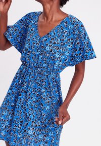 Blauwe bloemenjurk met korte mouwen, V-hals en een elastische taille. Bevat kleine meerkleurige bloemen op een gestructureerde achtergrond.
