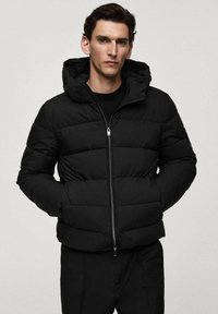Sort pufferjakke med en tætsiddende silhuet, vandret quiltet design, front lynlås og en justerbar hætte. Blød tekstur, minimalistisk stil.