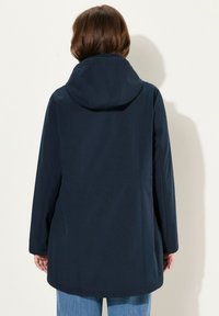 Tummansininen, hupullinen takki, jonka pinta on silkkinen ja siinä on saumatarkoituksia sekä rento istuvuus. Pitkät hihat ja lantiolle ylettyvä leikkaus.