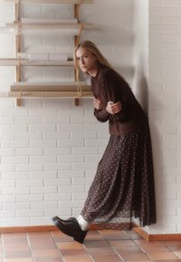 Brown long-sleeve top with round neckline, paired with a brown polka dot skirt and black shoes. Smooth textures and layered design are visible.